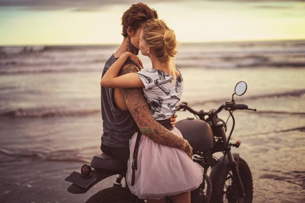 Pareja apasionada abrazándose en motocicleta en la playa del océano durante el hermoso amanecer - foto de stock