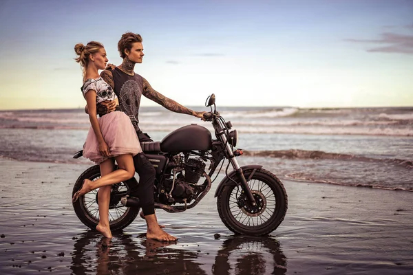 Парень обнимает подружку и сидит на мотоцикле на берегу океана — стоковое фото