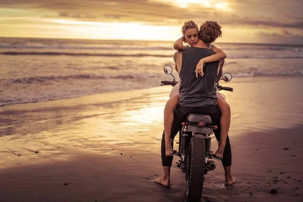 Heterosexual couple hugging on motorcycle on ocean beach during beautiful sunrise — Stock Photo