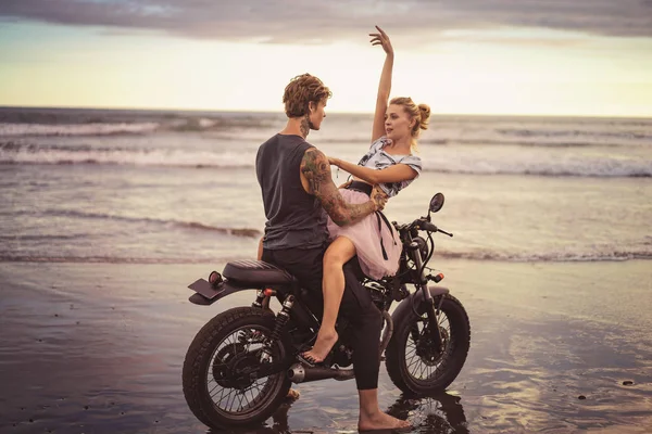 Pareja joven abrazándose en motocicleta en la playa del océano durante el hermoso amanecer - foto de stock