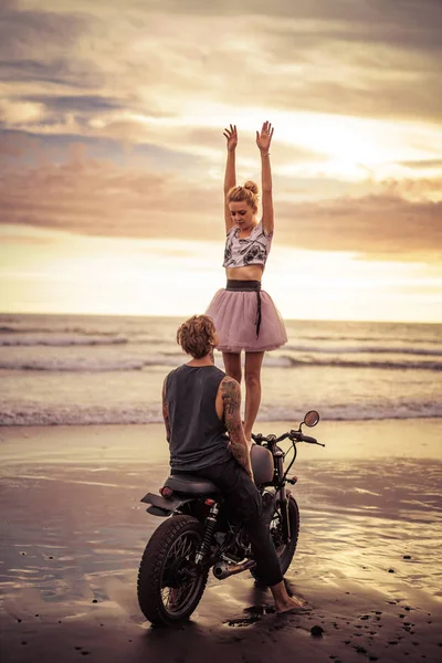 Happy girlfriend standing on motorcycle with hands up on ocean beach — Stock Photo