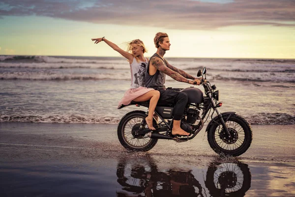 Happy boyfriend and girlfriend riding motorbike on seashore during sunrise — Stock Photo