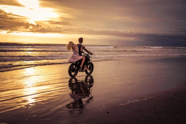 Вид ззаду хлопець і дівчина катаються на мотоциклі на океанічному пляжі під час сходу сонця — стокове фото