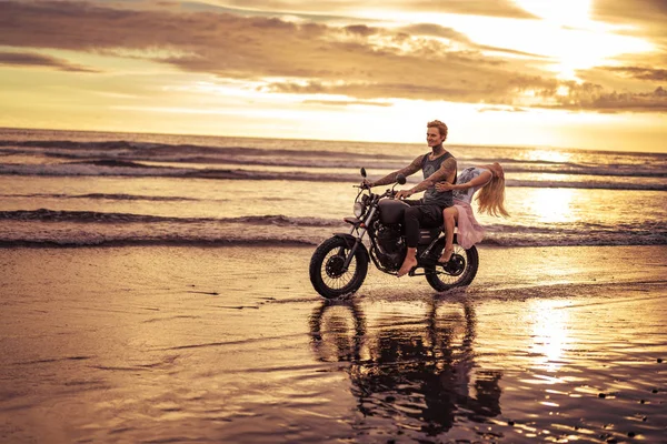 Cariñoso novio y novia a caballo motocicleta en la playa del océano durante el amanecer - foto de stock