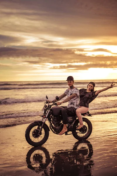 Feliz casal equitação motocicleta na praia durante o nascer do sol — Fotografia de Stock