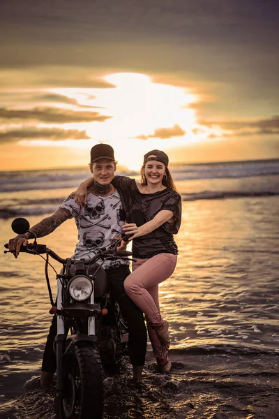 Smiling couple with motorcycle on ocean beach — Stock Photo