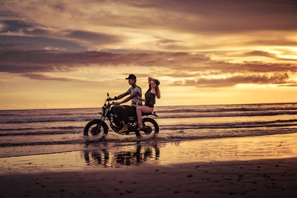 Affectionate couple riding motorcycle on ocean beach — Stock Photo