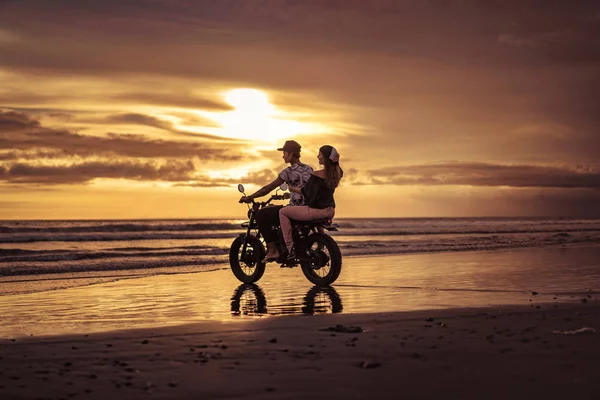 Casal andando de moto no oceano durante o nascer do sol — Fotografia de Stock