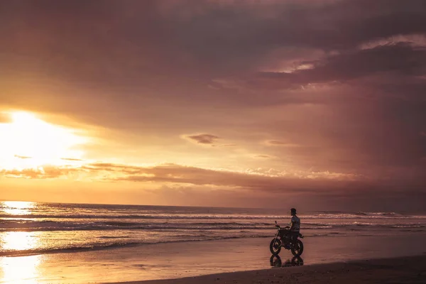 Man sitting on motorbike on seashore and looking at beautiful sunset — Stock Photo