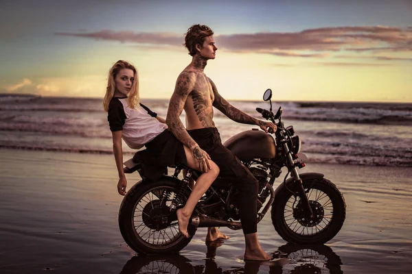 Couple posing on motorcycle on ocean beach — Stock Photo