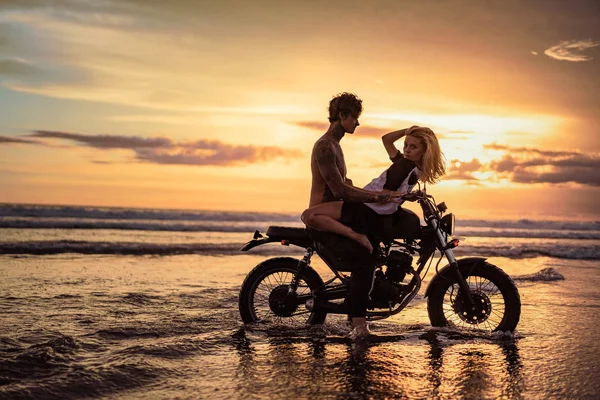Вид збоку пристрасна пара на мотоциклі на пляжі під час заходу сонця — стокове фото