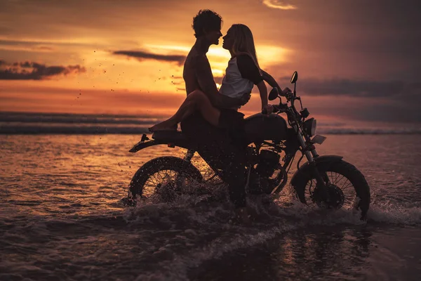 Pareja apasionada abrazándose en moto en la playa durante el atardecer - foto de stock