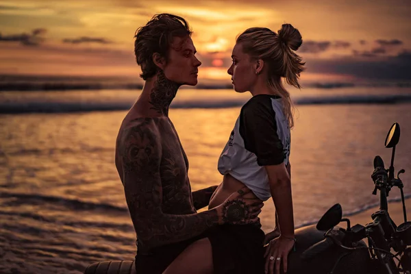 Casal apaixonado abraçando na motocicleta na praia durante o pôr do sol — Fotografia de Stock