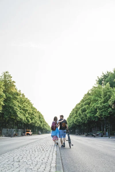 Rear view of couple of tourists with backpacks and bicycle walking at street in Berlin, Germany — Stock Photo