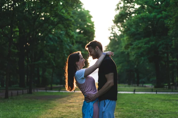 Vista lateral de casal sorridente abraçando uns aos outros no prado no parque — Fotografia de Stock