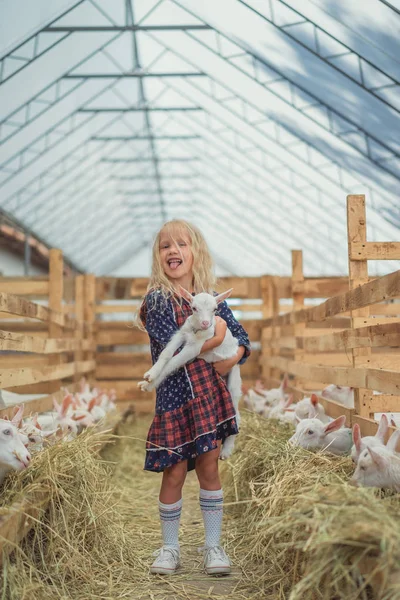 Entzückendes Kind streckt Zunge aus und hält Ziege auf Bauernhof — Stockfoto
