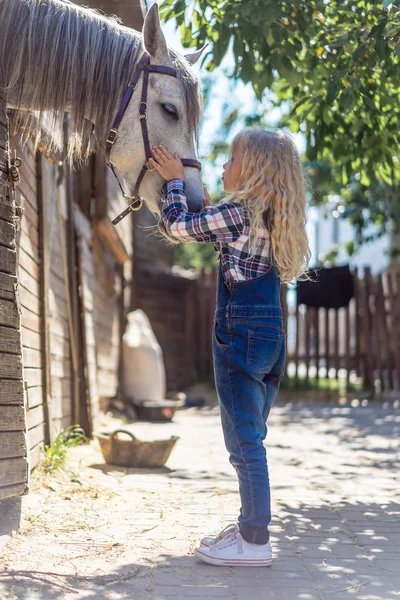 Vista lateral da criança vai beijar cavalo branco na fazenda — Fotografia de Stock