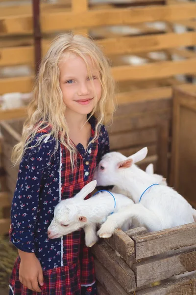 Criança sorrindo de pé no celeiro com cabras pequenas — Fotografia de Stock