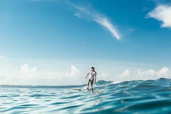Vista distante do surfista masculino montando em prancha de surf no oceano em Nusa Dua Beach, Bali, Indonésia — Fotografia de Stock