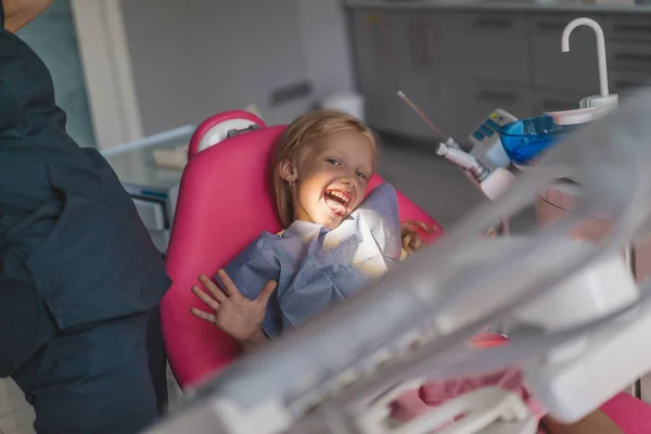 Visão parcial do dentista e da criança colando a língua na cadeira no consultório do dentista — Fotografia de Stock