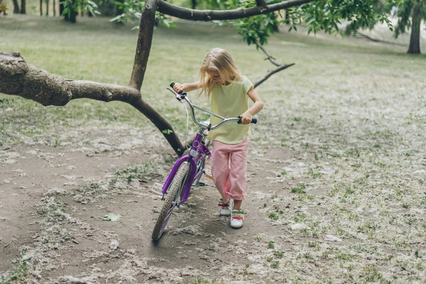 Niño con bicicleta de pie cerca de la rama del árbol en el parque - foto de stock