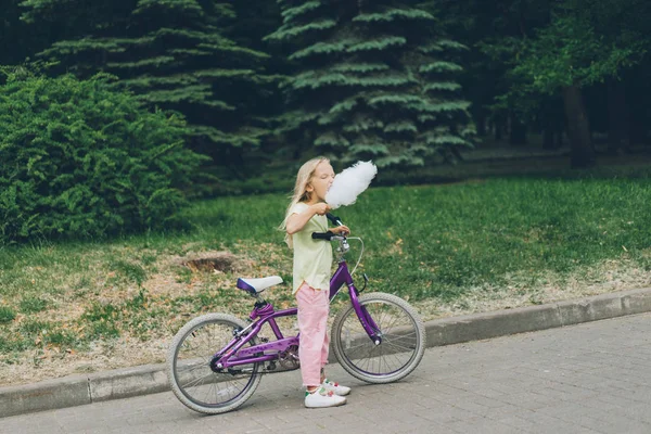 Side view of adorable kid with bicycle eating cotton candy in park — Stock Photo