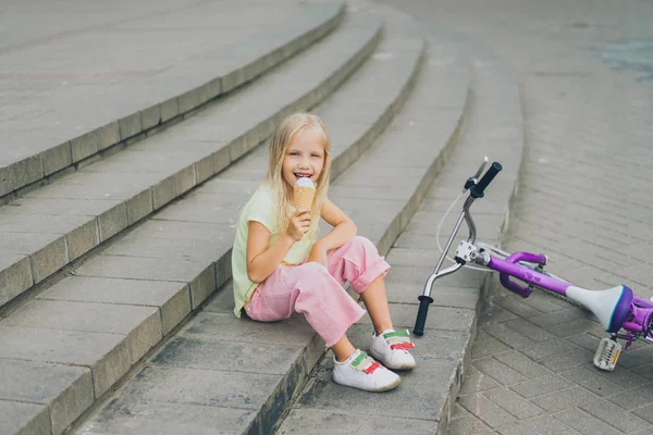 Lindo niño comiendo helado mientras está sentado en la ciudad pasos cerca de la bicicleta solo - foto de stock