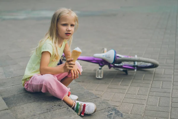 Lindo niño con helado sentado en los escalones de la ciudad cerca de la bicicleta solo - foto de stock