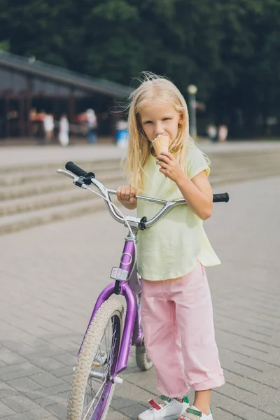 Adorable little kid with ice cream and bicycle standing on city street — Stock Photo