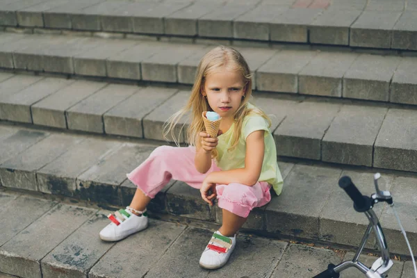 Mignon enfant avec crème glacée assis sur les marches de la ville seul — Photo de stock