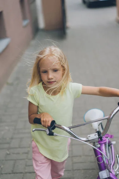 Portrait of little child with bicycle walking on street — Stock Photo