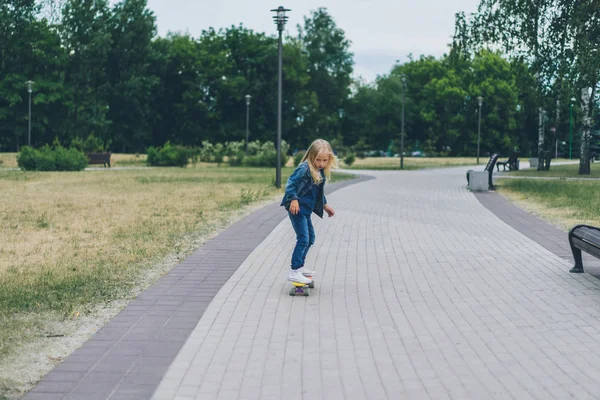 Cute little child in denim clothing skating on skateboard in park — Stock Photo