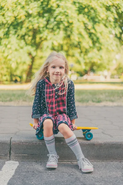 Счастливый ребенок сидит на скейтборде и смотрит в камеру на городской улице — стоковое фото