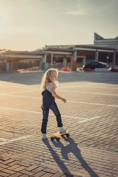 Rear view of adorable kid standing with skateboard at parking lot — Stock Photo