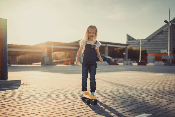 Smiling adorable kid standing with skateboard at parking lot — Stock Photo