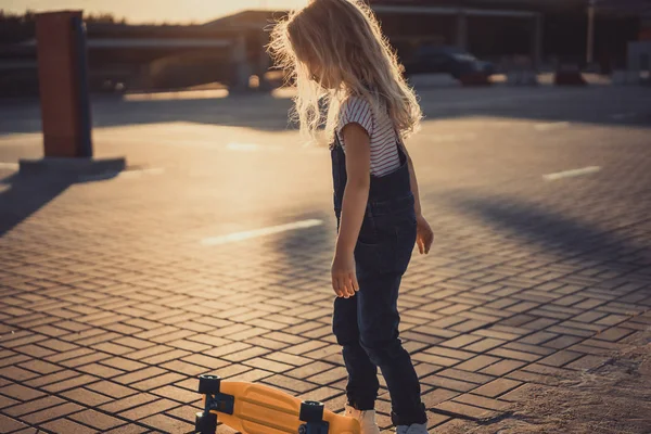 Вид збоку маленької дитини, що стоїть біля скейтборду на парковці — Stock Photo