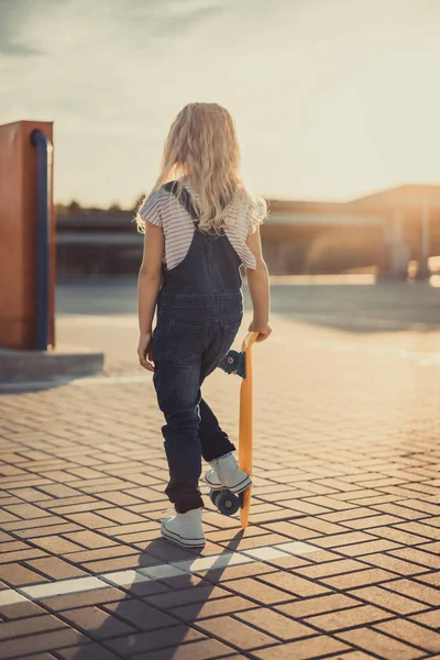 Rear view of little kid standing with penny board at parking lot — Stock Photo