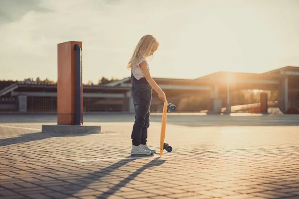 Вид сбоку маленького ребенка, стоящего с доской на парковке — стоковое фото
