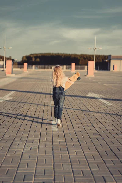 Visão traseira da criança caminhando com skate no estacionamento — Fotografia de Stock