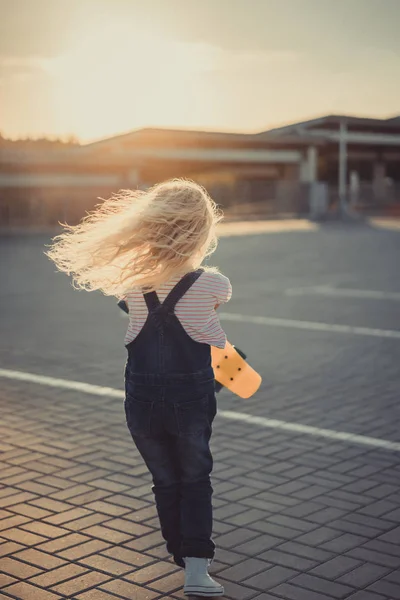 Rückansicht von kleinem Kind, das mit Skateboard auf Parkplatz läuft — Stockfoto