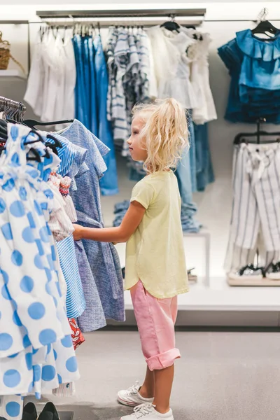 Vue latérale de adorable petit enfant choisir des vêtements dans la boutique — Photo de stock