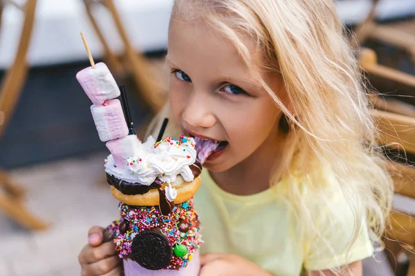 Porträt eines entzückenden kleinen Kindes, das in die Kamera blickt und köstliches Dessert isst — Stockfoto