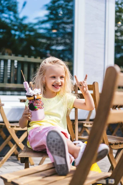 Selektiver Fokus des glücklichen liebenswerten Kindes, das Rock-Geste macht und köstliches Dessert im Café hält — Stockfoto