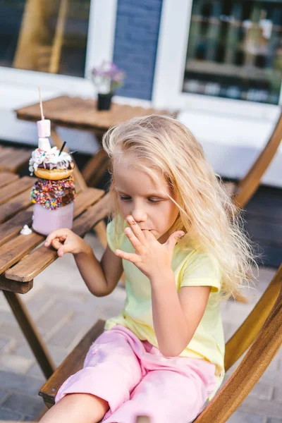 Enfoque selectivo de niños pequeños lamiendo los dedos mientras están sentados en la mesa con delicioso postre en la cafetería - foto de stock