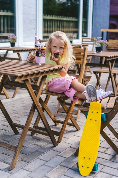 Selective focus of little child eating dessert at table near skateboard in cafe — Stock Photo