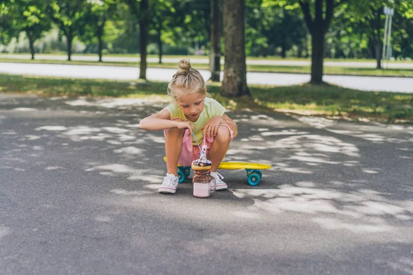 Messa a fuoco selettiva del bambino seduto sullo skateboard e mangiare dessert in strada — Foto stock