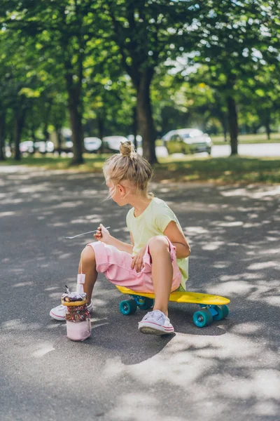 Side view of little child sitting on skateboard in front of dessert at street — Stock Photo