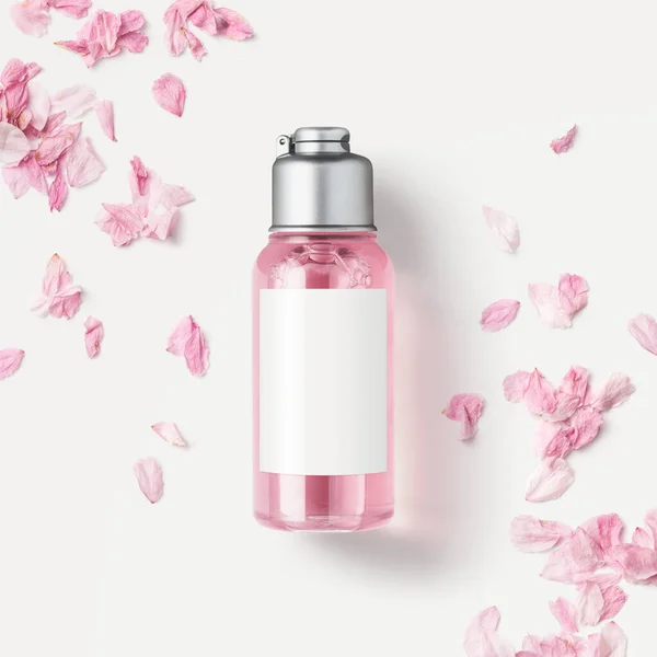 cosmetics / skin care product packaging design concept or mockup with small bottle with pink liquid soap or shower gel surrounded by delicate pink flower petals, blank white label for your design