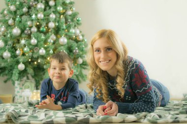 Mutlu anne ve çocuk battaniye üzerinde yalan ve süslenmiş noel ağacının önünde gülümseyerek