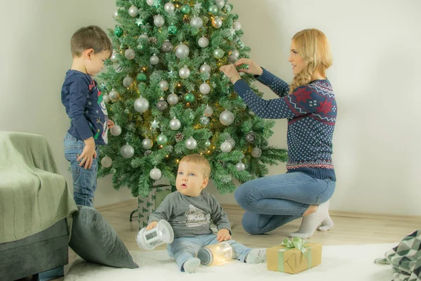 Mother and older son decorated Christmas tree when baby son playing with lantern on the floor